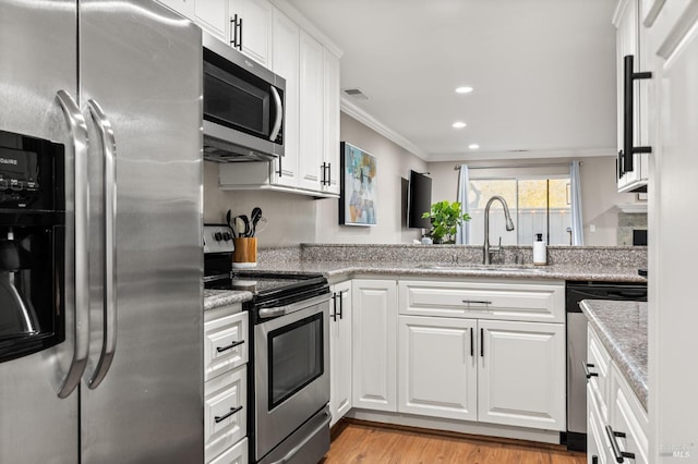 kitchen featuring sink, appliances with stainless steel finishes, light stone countertops, light hardwood / wood-style floors, and white cabinets