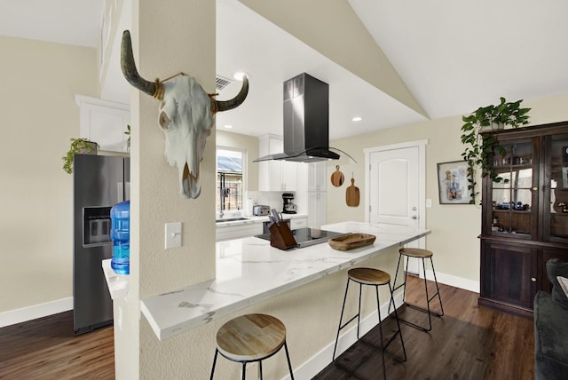 kitchen featuring light stone counters, island exhaust hood, stainless steel fridge, white cabinetry, and a kitchen bar