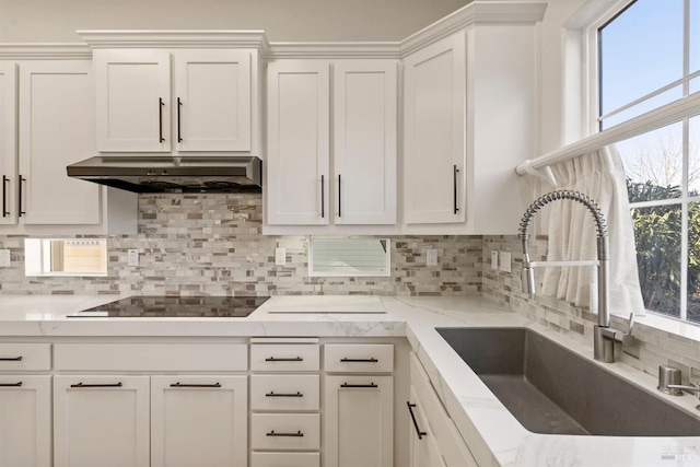 kitchen with sink, white cabinetry, black electric cooktop, light stone countertops, and backsplash