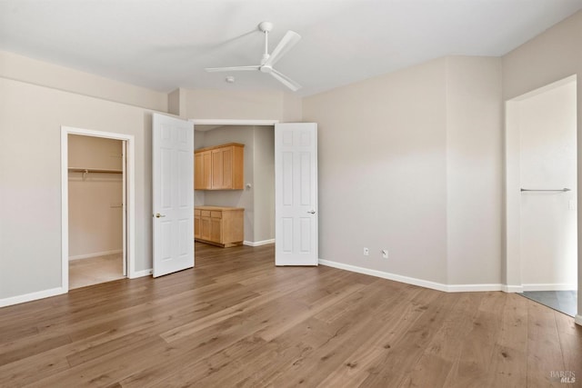 unfurnished bedroom featuring hardwood / wood-style flooring, a walk in closet, a closet, and ceiling fan