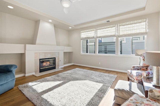 living room featuring a tiled fireplace, hardwood / wood-style flooring, and a tray ceiling