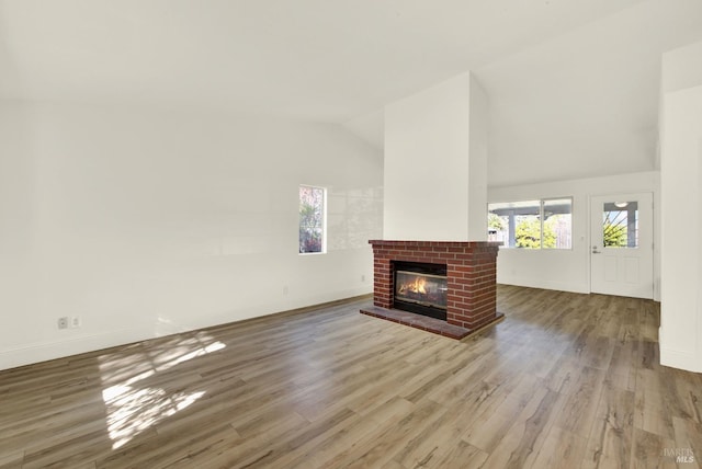 unfurnished living room with vaulted ceiling, hardwood / wood-style floors, and a brick fireplace