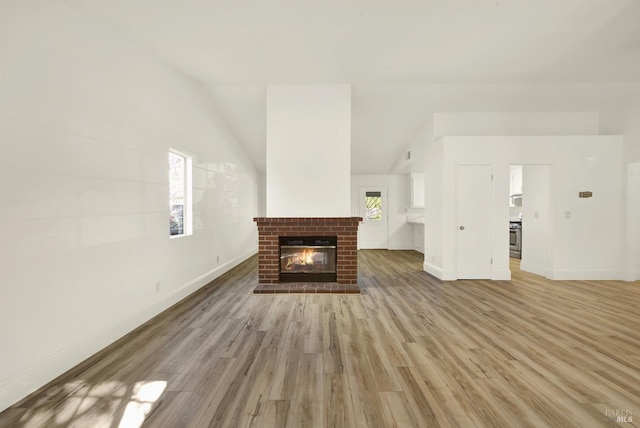 unfurnished living room with lofted ceiling, a fireplace, and light wood-type flooring