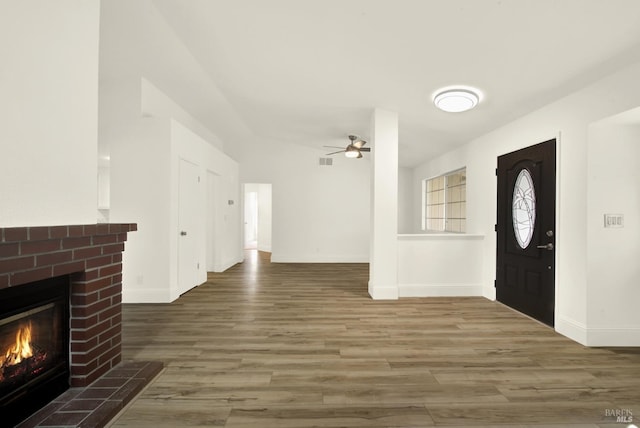 foyer entrance featuring a brick fireplace, dark hardwood / wood-style floors, and ceiling fan