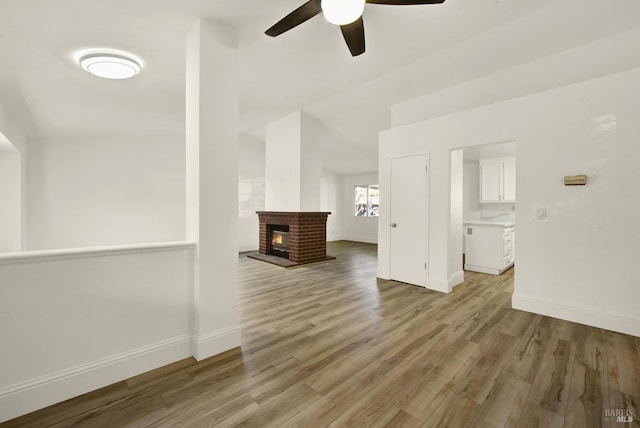 unfurnished living room with ceiling fan, a brick fireplace, and light wood-type flooring