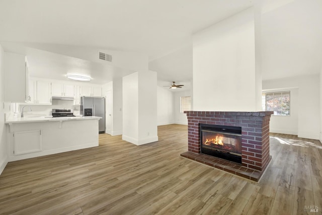 unfurnished living room featuring sink, ceiling fan, a brick fireplace, vaulted ceiling, and light wood-type flooring