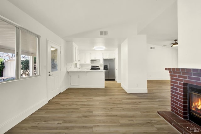 kitchen featuring a fireplace, wood-type flooring, white cabinets, kitchen peninsula, and stainless steel appliances