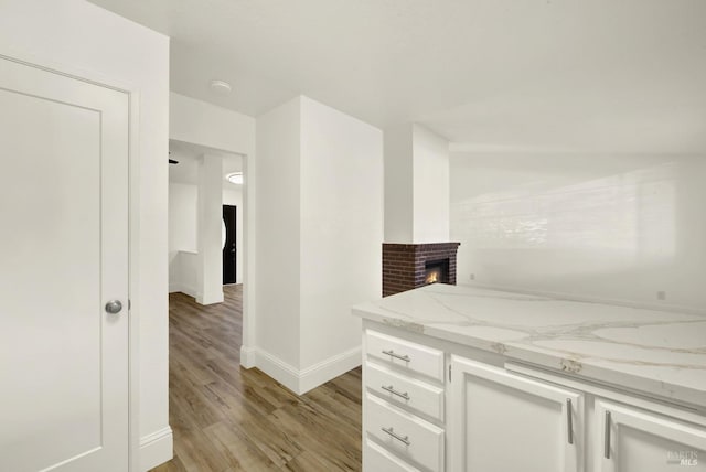 kitchen with sink, a fireplace, light stone countertops, light hardwood / wood-style floors, and white cabinets