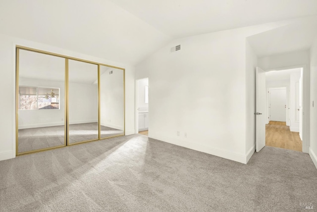 unfurnished bedroom with vaulted ceiling, light colored carpet, and a closet