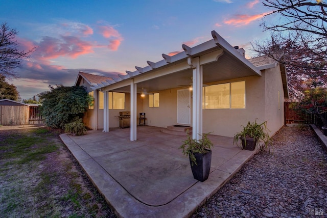 back house at dusk featuring ceiling fan and a patio