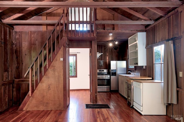 kitchen featuring stainless steel appliances, white cabinetry, hardwood / wood-style flooring, and wooden walls