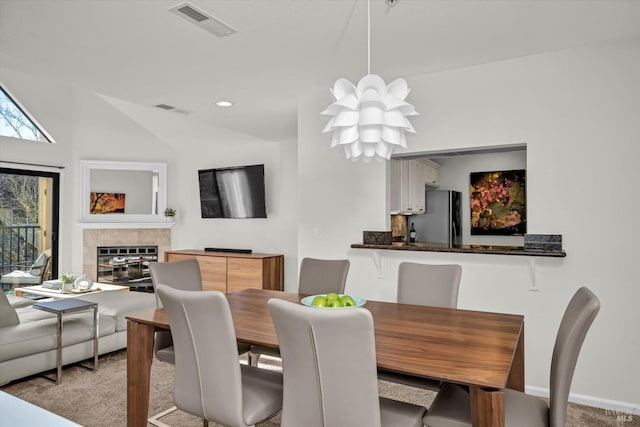 carpeted dining space with vaulted ceiling and a tile fireplace