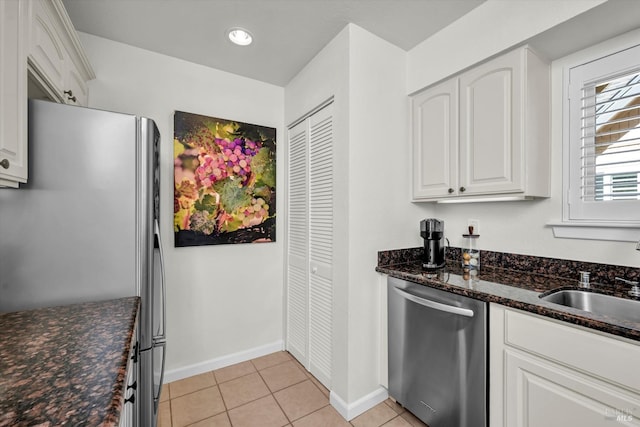 kitchen featuring sink, light tile patterned floors, appliances with stainless steel finishes, dark stone countertops, and white cabinets