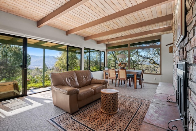 sunroom / solarium featuring a mountain view, a stone fireplace, wooden ceiling, and beamed ceiling