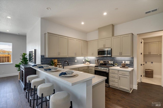 kitchen with appliances with stainless steel finishes, backsplash, a kitchen breakfast bar, kitchen peninsula, and dark wood-type flooring