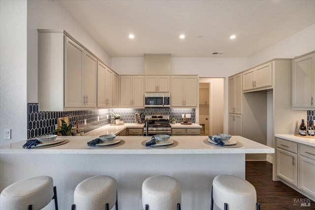 kitchen with appliances with stainless steel finishes, dark hardwood / wood-style floors, backsplash, and a kitchen bar