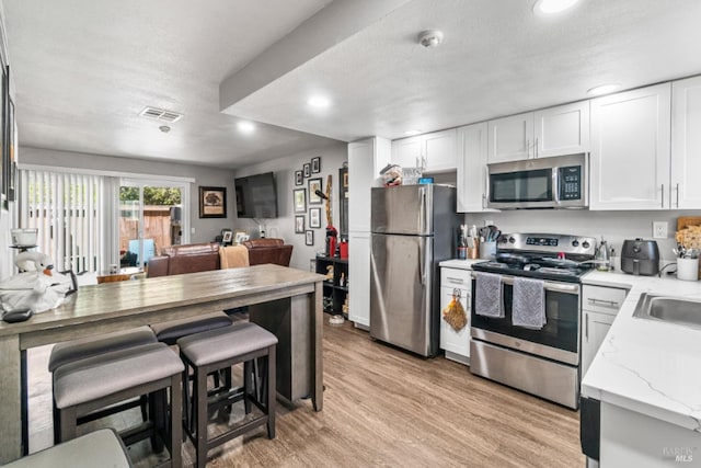 kitchen featuring white cabinetry, light wood-type flooring, a textured ceiling, and appliances with stainless steel finishes