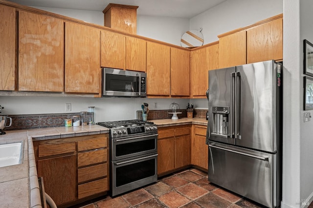 kitchen featuring stainless steel appliances, lofted ceiling, sink, and tile counters