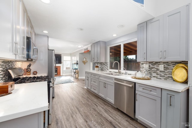 kitchen with sink, gray cabinetry, backsplash, stainless steel appliances, and light hardwood / wood-style flooring