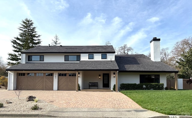 traditional-style house with decorative driveway, roof with shingles, covered porch, a front yard, and a garage