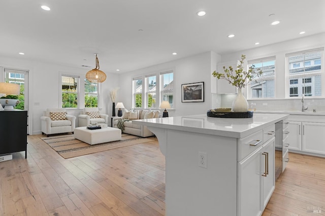 kitchen featuring light countertops, backsplash, light wood-style floors, white cabinets, and a sink