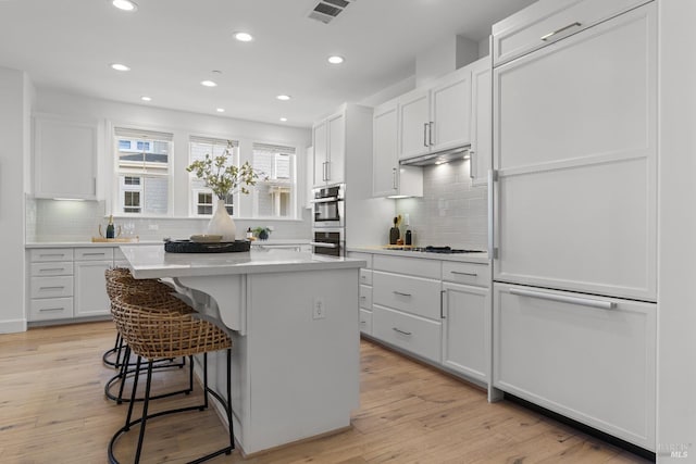 kitchen with a center island, light wood-style flooring, white gas cooktop, white cabinets, and a kitchen bar