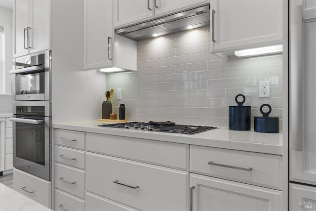 kitchen featuring stainless steel appliances, backsplash, white cabinetry, and under cabinet range hood