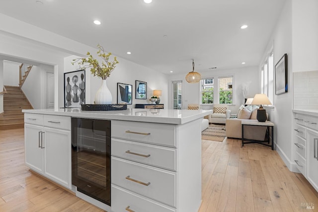 kitchen featuring wine cooler, a center island, light countertops, light wood-type flooring, and white cabinetry