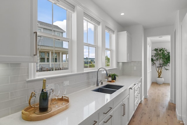 kitchen featuring light wood finished floors, light stone counters, a sink, white cabinetry, and backsplash