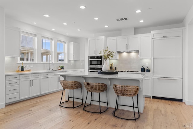 kitchen with a center island, a breakfast bar area, stainless steel double oven, white cabinetry, and a sink