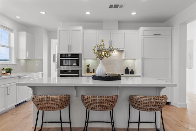 kitchen with double oven, visible vents, white cabinets, and light wood-style flooring