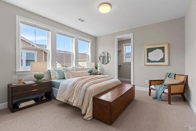 bedroom featuring light carpet, a closet, a walk in closet, and baseboards