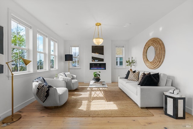 living area featuring hardwood / wood-style floors, a glass covered fireplace, and baseboards