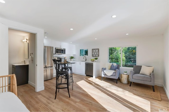 interior space featuring a breakfast bar, sink, white cabinetry, appliances with stainless steel finishes, and light hardwood / wood-style floors