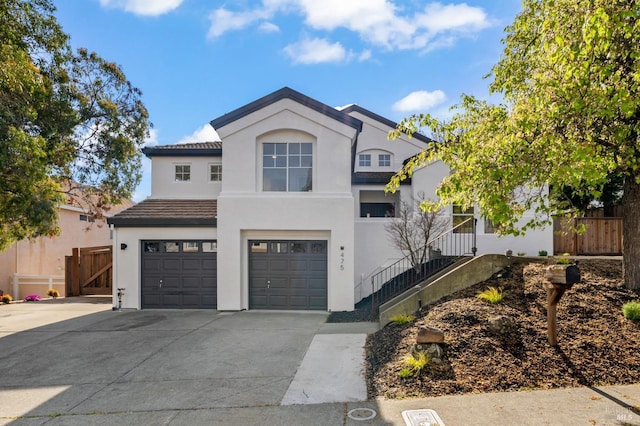 view of front of house with driveway, a garage, a tiled roof, fence, and stucco siding