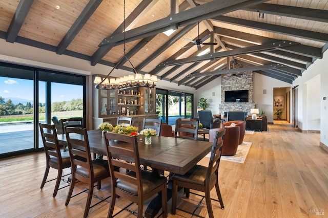 dining space featuring a stone fireplace, high vaulted ceiling, beamed ceiling, ceiling fan, and light hardwood / wood-style floors