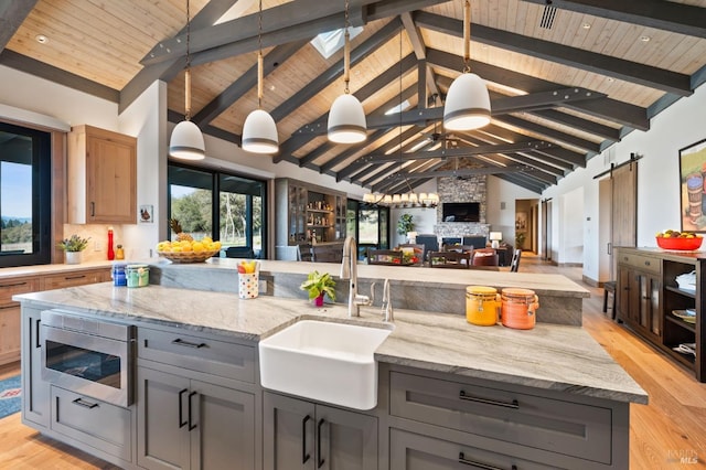 kitchen with light stone counters, stainless steel microwave, beamed ceiling, and pendant lighting