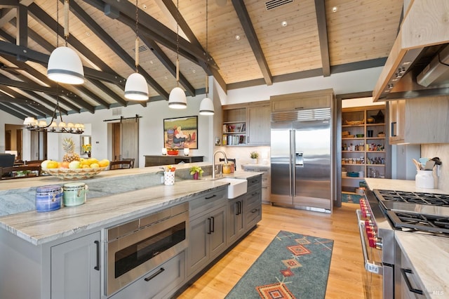 kitchen featuring gray cabinets, premium range hood, beam ceiling, built in appliances, and a barn door