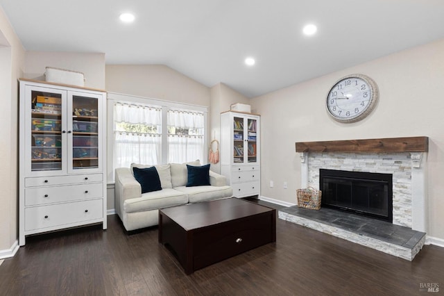 living room with dark hardwood / wood-style floors, vaulted ceiling, and a stone fireplace