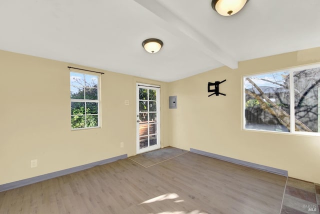 empty room featuring beamed ceiling, hardwood / wood-style flooring, and electric panel