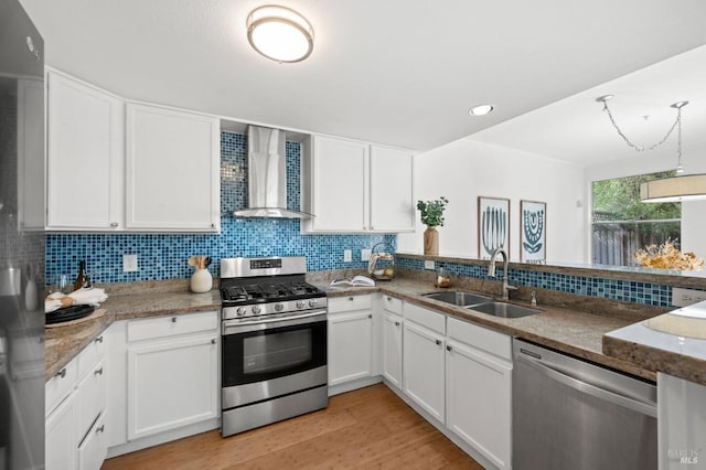 kitchen with wall chimney range hood, stainless steel appliances, sink, and white cabinets