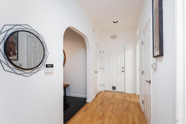 hall featuring baseboards, recessed lighting, arched walkways, and light wood-style flooring