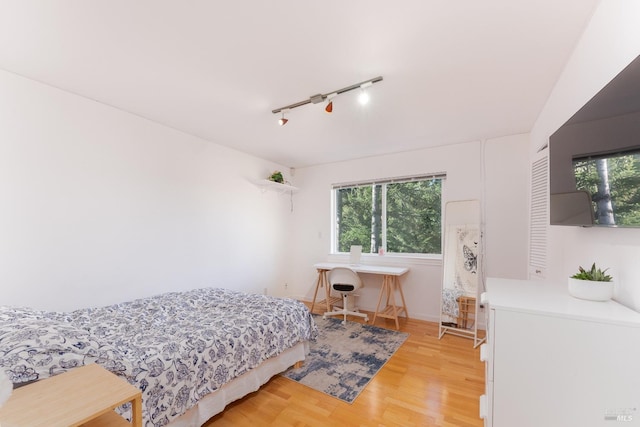 bedroom with track lighting, baseboards, and light wood-style floors