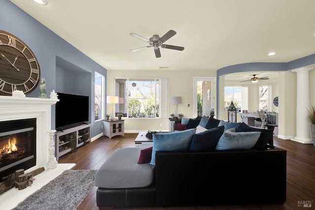 living room with dark wood-type flooring, ceiling fan, and ornate columns