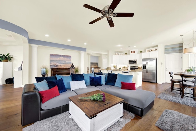 living room with decorative columns, ceiling fan, and light wood-type flooring