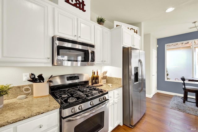 kitchen featuring light stone countertops, white cabinetry, appliances with stainless steel finishes, and light wood-type flooring