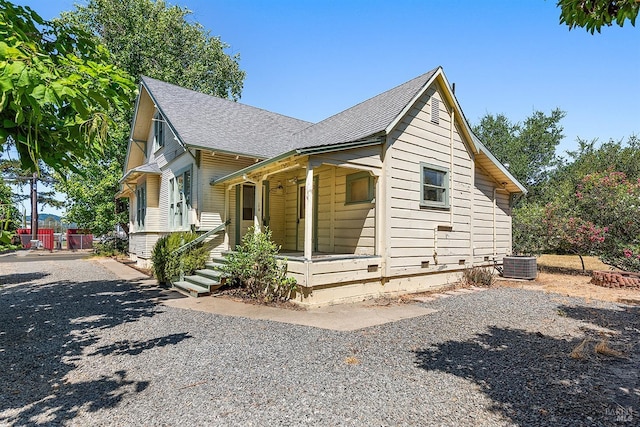 bungalow-style house featuring a shingled roof, covered porch, and central air condition unit