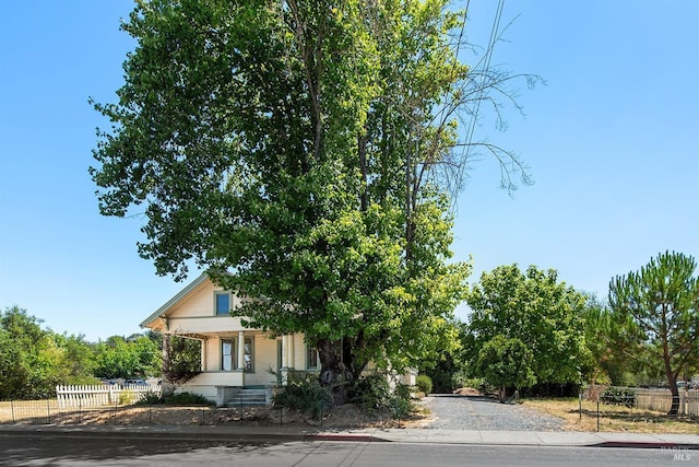 obstructed view of property featuring covered porch, gravel driveway, and fence