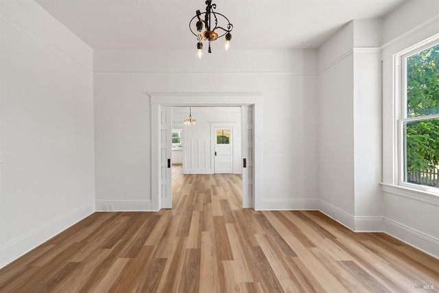 unfurnished dining area with light wood-type flooring, baseboards, and a chandelier