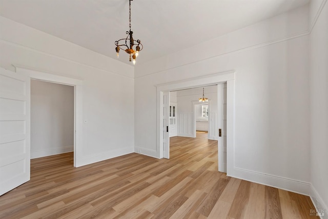 empty room featuring baseboards, a chandelier, and light wood finished floors